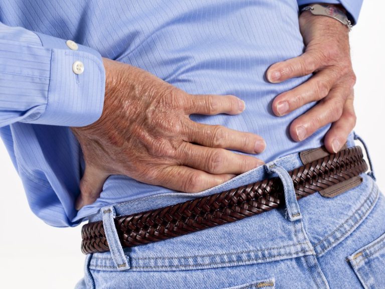 Image of older human with light blue clothes holding their low back as if in pain at L5/S1 bilaterally. 